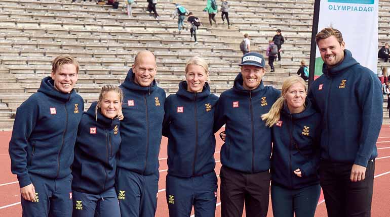 Sju olympier från olika idrotter håller om varandra och ler inne på Stockholms Olympiastadion. 
