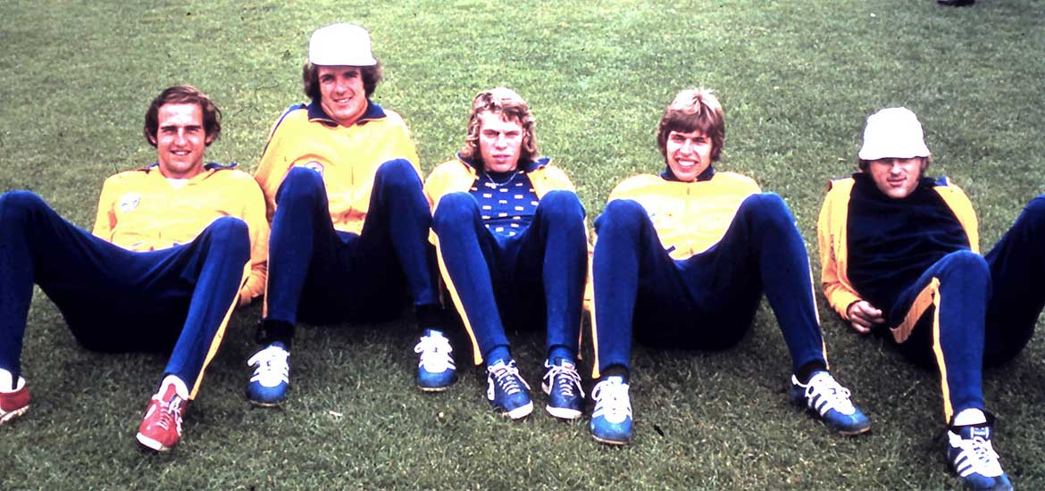 Fem grabbar som sitter i gräset med blågula kläder. 