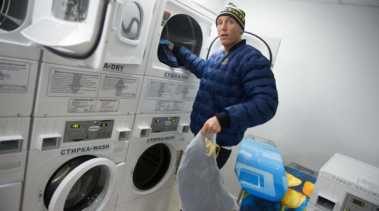 Skidskytten Björn Ferry står i ett rum fullt med tvättmaskiner och en påse tvätt i handen. 
