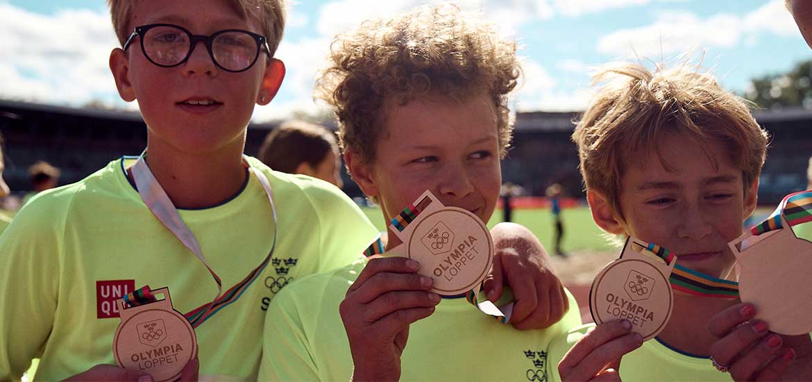 Barn som visar upp en medalj med Olympialoppet runt halsen. 