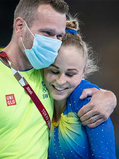 En tränare med munskydd kramar om en glad gymnast.