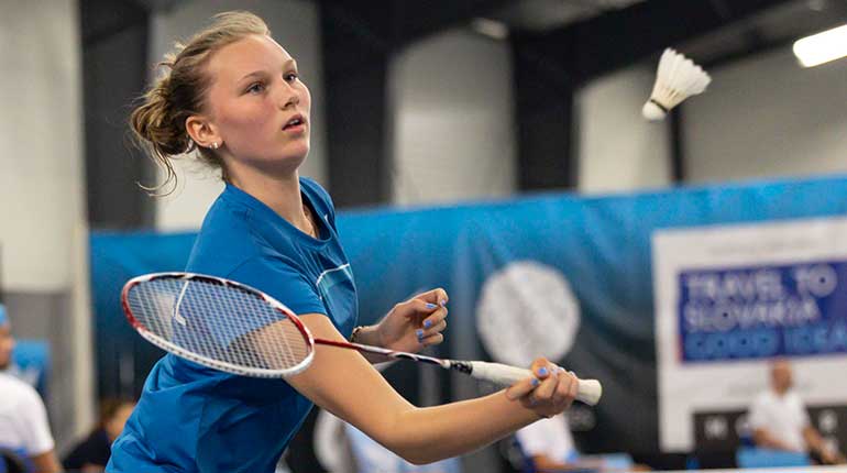 Närbild på Sofia Strömvall i blå tröja med ett badmintonracket och en boll som flyger iväg åt höger. 