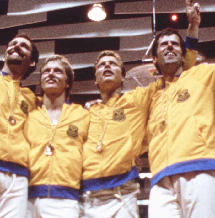 Fyra glada killar i svenska kläder som kramar om varandra. 
